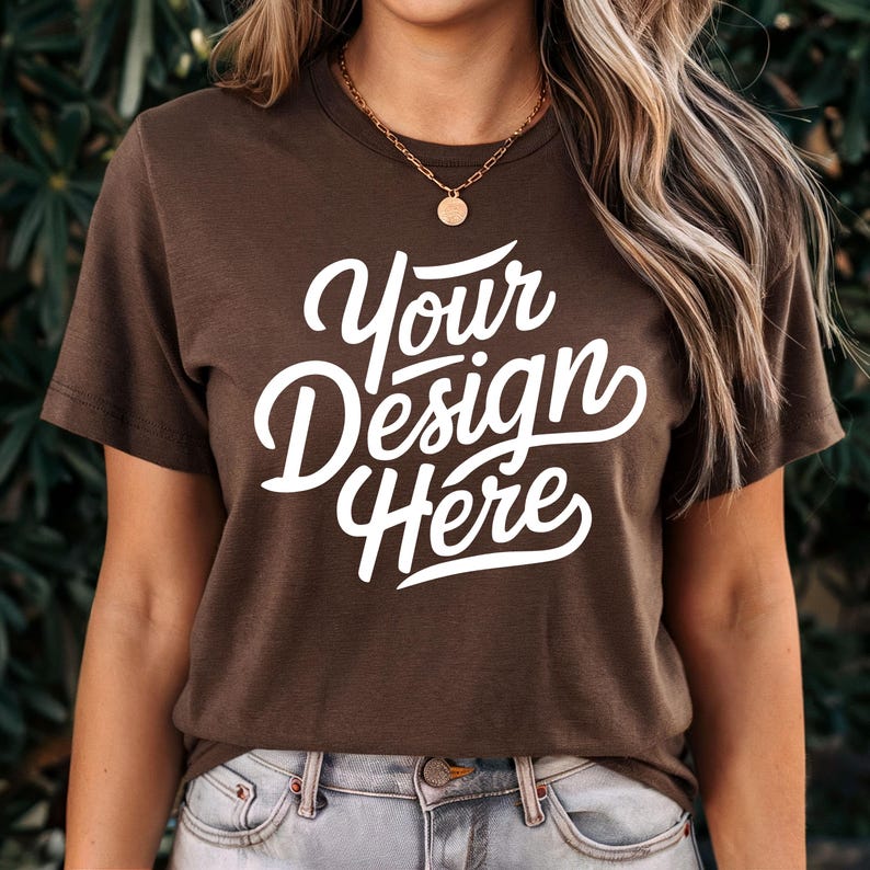 May include: A brown t-shirt with the text "Your Design Here" in white lettering. The shirt is being modelled by a person with long brown hair.