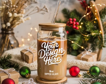 Puede incluir: Un vaso transparente con tapa y pajita de madera, lleno de una bebida de café. La taza tiene el texto "Your Design Here" y "16 oz Sipper Glass" en blanco. La taza está sobre un posavasos de madera, rodeada de adornos y regalos navideños.