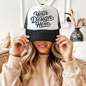 Könnte beinhalten: Eine weiße und schwarze Trucker-Kappe mit schwarzem Netzrücken. Die Vorderseite der Kappe trägt den Text "Your Design Here" in schwarzer Kursivschrift.