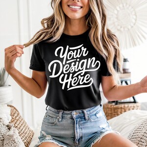 May include: Black t-shirt with the text "Your Design Here" in white script. The shirt is short-sleeved and worn with denim shorts. The model is holding a strand of hair.