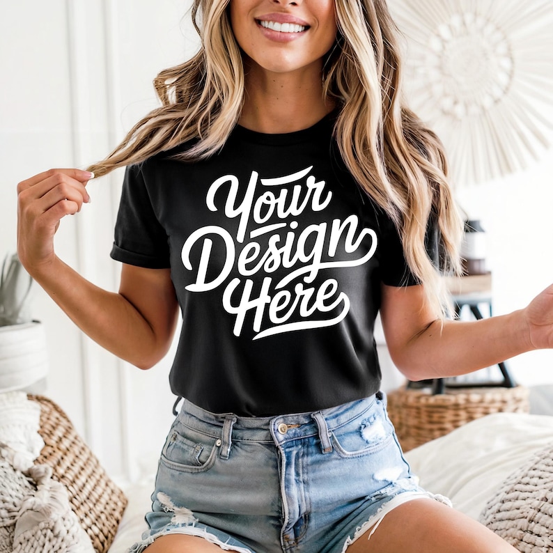 May include: Black t-shirt with the text "Your Design Here" in white script. The shirt is short-sleeved and worn with denim shorts. The model is holding a strand of hair.