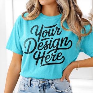 Puede incluir: Una camiseta turquesa con el texto "Your Design Here" en escritura negra. La camiseta de manga corta está hecha de un material suave y es de color liso. La camiseta se combina con unos vaqueros azules.