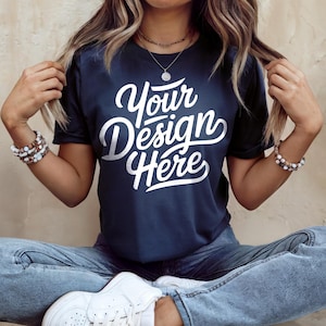 May include: Navy blue t-shirt with the text "Your Design Here" in white script. The model is wearing blue jeans and white sneakers. The person is also wearing bracelets and a necklace.