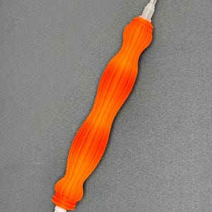 May include: An orange and yellow diamond painting pen with a ribbed handle. The pen has a clear plastic tip and a gold-coloured metal tip. The pen is designed for precision and detail work in diamond painting projects.