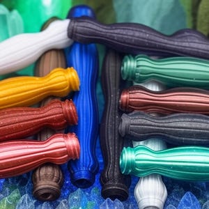 May include: A collection of colorful, textured pens with a ribbed design. The pens are arranged in a row, with the tips facing the viewer. The pens are made of different materials, including metal, plastic, and wood.