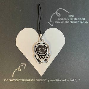 May include: A clear acrylic charm with a black cord, featuring a cartoon astronaut design. The charm is attached to a silver-colored metal clasp. The charm is placed on a white heart-shaped cutout, with text indicating it's a rare item.