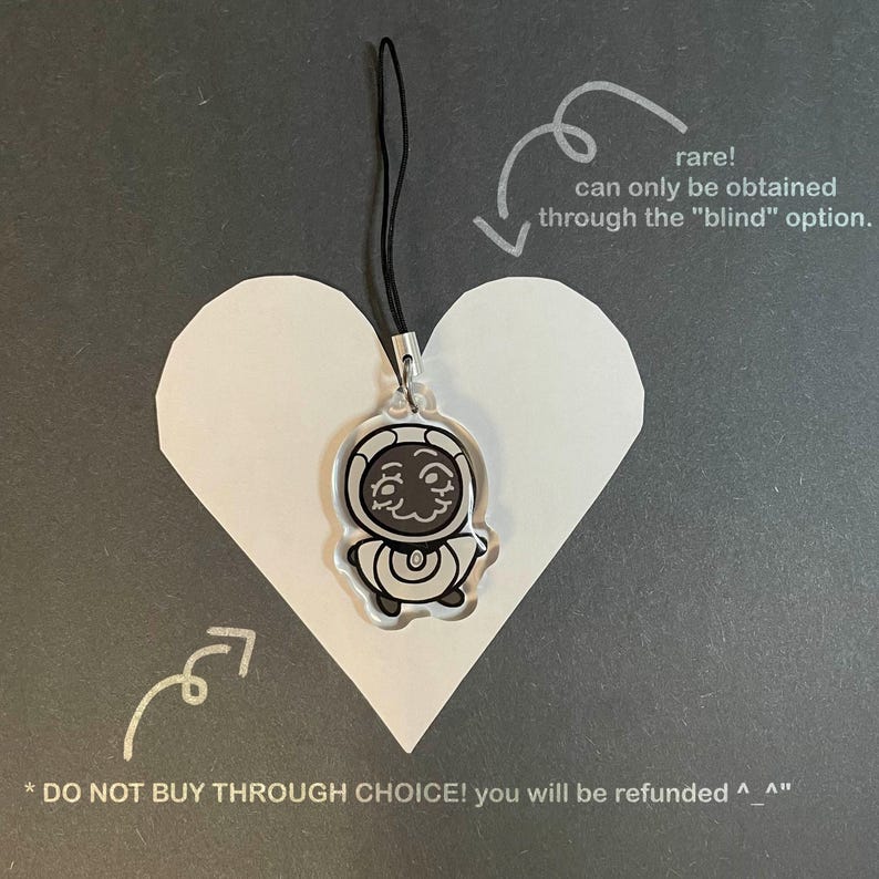 May include: A clear acrylic charm with a black cord, featuring a cartoon astronaut design. The charm is attached to a silver-colored metal clasp. The charm is placed on a white heart-shaped cutout, with text indicating it's a rare item.