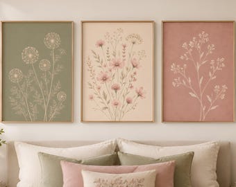 May include: Three rectangular wall art prints in thin wooden frames. The left print features white dandelion illustrations on a sage green background. The center print shows pink wildflowers on a cream background. The right print displays white floral stems on a dusty rose background.