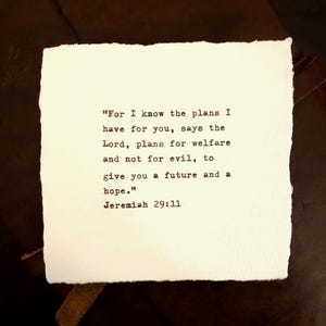 May include: A square piece of off-white paper with deckled edges featuring black typewriter-style text that reads: "For I know the plans I have for you, says the Lord, plans for welfare and not for evil, to give you a future and a hope." Jeremiah 29:11.