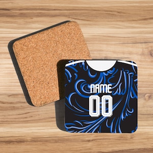 Op de afbeelding: Vierkante onderzetter met een zwarte achtergrond en blauw bloemmotief. De onderzetter heeft het woord "NAME" en het nummer "00" in het wit. Ernaast ligt een aparte kurken onderzetter.