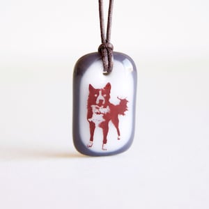 May include: A brown cord necklace with a gray and white rectangular pendant featuring a red silhouette of a dog.