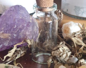 May include: A small, clear glass bottle with a cork stopper. The bottle is surrounded by various crystals and dried herbs. The bottle is labeled "Devil's Spirit (Viburnum)" and "AKA "C". Used for Protection; clear away; better business; money"