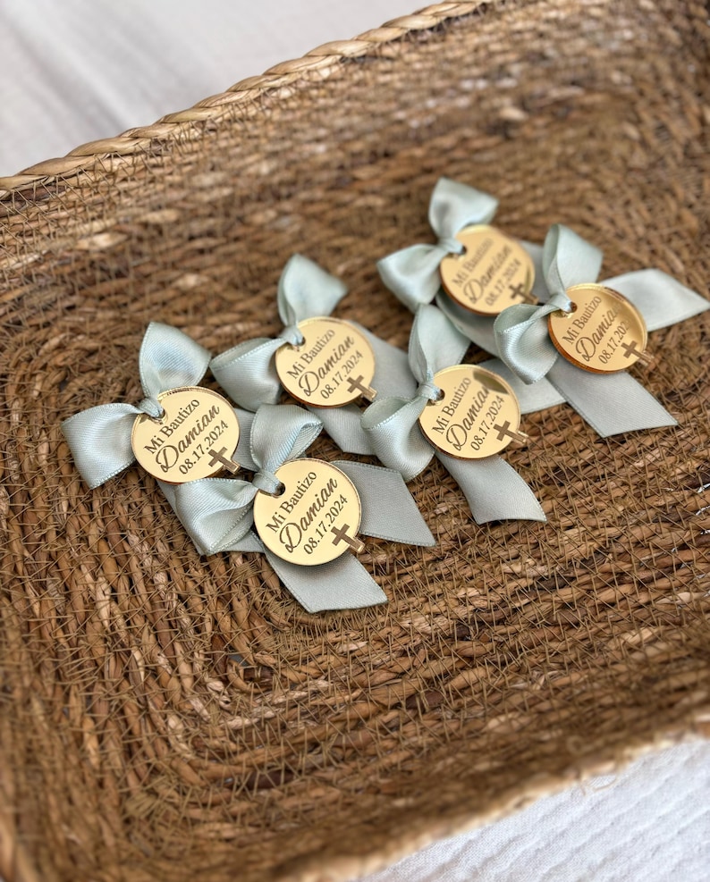 K&ouml;nnte beinhalten: Ein Korb gef&uuml;llt mit goldenen runden Gef&auml;lligkeiten mit blauen Schleifen. Jede Gef&auml;lligkeit tr&auml;gt den Text "Mi Bautizo Damian 08.17.2024" und ein kleines Kreuz.