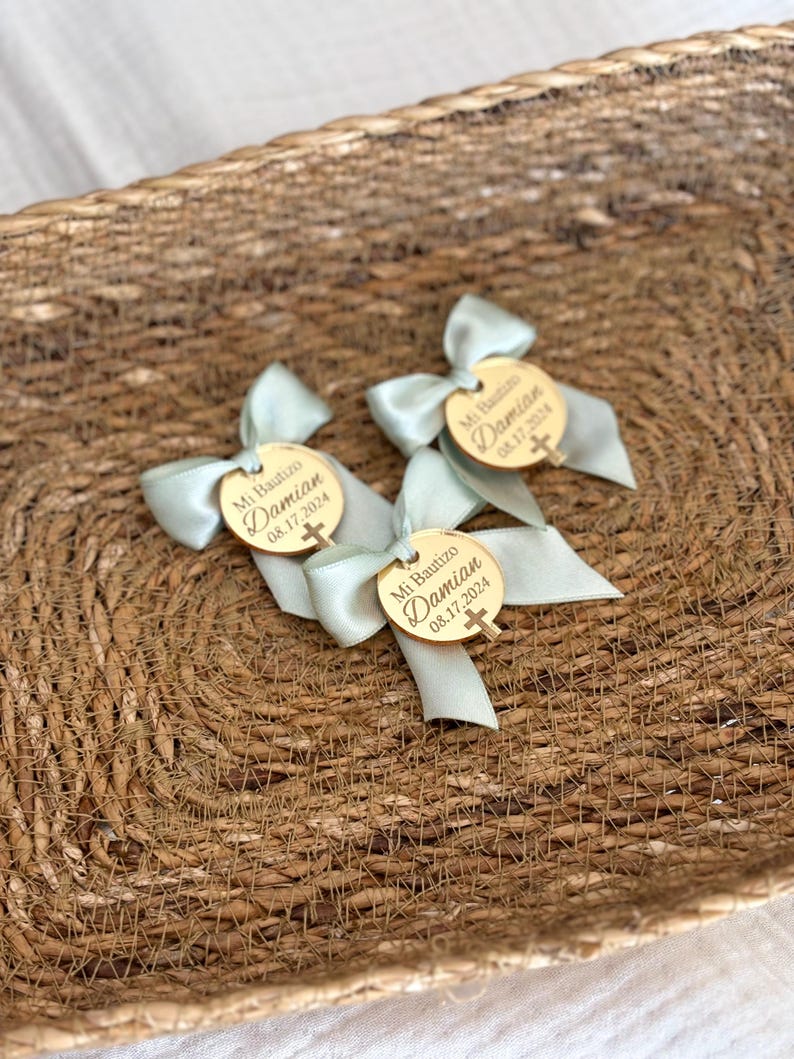 K&ouml;nnte beinhalten: Ein Korb gef&uuml;llt mit hellblauen und goldenen Taufgeschenken. Jedes Geschenk ist ein kleiner Holzkreis mit dem Text "Mi Bautizo Damian 08.17.2024" und einem kleinen goldenen Kreuz.