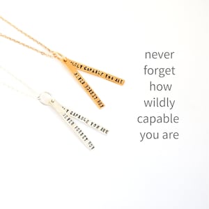 Può includere: Due collane d'oro con un ciondolo che recita "wildly capable you are" e "never forget how".