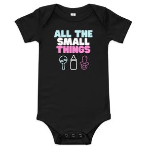 May include: Black baby bodysuit with the text "ALL THE SMALL THINGS" in blue, white, and pink. Below the text are illustrations of a rattle, a baby bottle, and a pacifier, all in white with blue and pink accents.