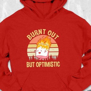 May include: Red hooded sweatshirt with the text "Burnt Out But Optimistic" and a cartoon image of a burning marshmallow.