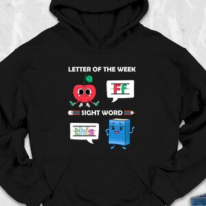 May include: Black hooded sweatshirt with a white graphic of a red apple with a letter F on it, a blue book with a letter F on it, and the text "Letter of the Week" and "Sight Word".