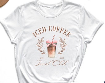 May include: White t-shirt with a brown graphic of a glass of iced coffee with a pink ribbon and the text "ICED COFFEE EST. 1982 Social Club".