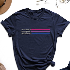 May include: A navy blue t-shirt with a graphic of a lightsaber in the colors of the bisexual pride flag.