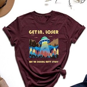 May include: Burgundy t-shirt with a graphic of a UFO over a forest with the text "Get in, loser. We're doing butt stuff."