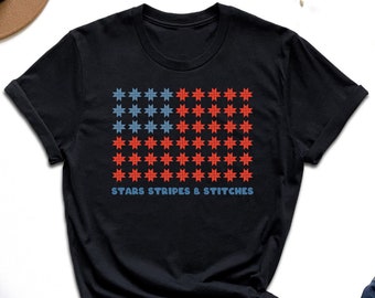 Puede incluir: Camiseta negra con un diseño de estrellas rojo, blanco y azul. El texto "Stars Stripes & Stitches" está impreso debajo del diseño.