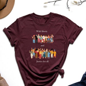 May include: A maroon t-shirt with a graphic of a diverse group of people and the text "With liberty and justice for all".