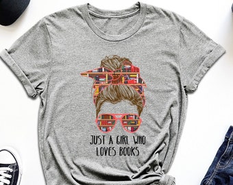 May include: Gray t-shirt with a graphic of a woman's hair styled in a messy bun with books in her hair and glasses. The text "Just a girl who loves books" is printed below the graphic.