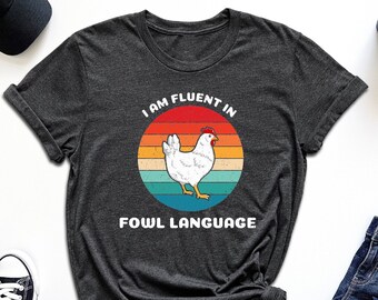 May include: A dark grey t-shirt with a retro-style graphic of a chicken and the text "I am fluent in fowl language".
