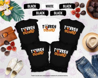 May include: A collection of black and white t-shirts with the text "TURKEY SQUAD" in white and orange. The shirts are arranged with a variety of accessories, including a brown leather bag, figs, a straw hat, and a pair of jeans.