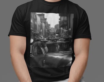 May include: Black t-shirt featuring a black and white image of three cats in a vintage car. The cats are wearing bandanas and appear to be holding something. The background shows a blurred city street.