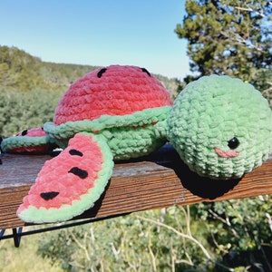 May include: A handmade crochet watermelon plushie with a red top, green rind, and black seed details. The plushie has a smiling face and is placed on a wooden surface. The overall theme is summer and fruit.