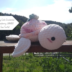May include: A crocheted strawberry sea turtle with a white body, pink and white shell, and a green stem. The turtle has a black eye and a pink stitched mouth. The text on the image reads "Berry Cute Crocheted Strawberry JUMBO Sea Turtle!"