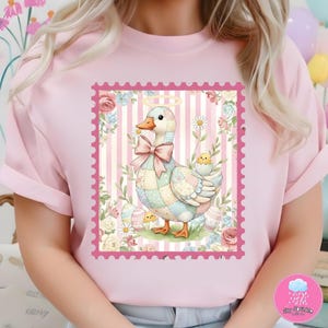 Op de afbeelding: Lichtroze T-shirt met een grillige illustratie van een patchwork gans met een halo en een roze strik, geplaatst in een roze postzegel kader. Het ontwerp bevat paaseieren, bloemen en een kuiken. Het shirt heeft een lichtroze kleur.