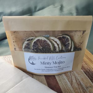 May include: A brown paper bag with a clear window, containing dried lime slices and green herbs. The bag has a label that reads "Minty Mojito Simmer Pot Kit" with the brand name "Mindful RN Creations".
