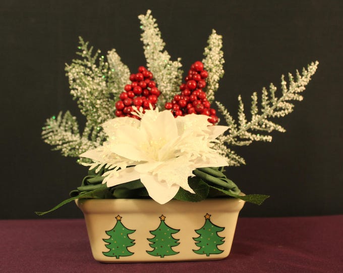 White Poinsettia, Green Roses, Red Berries, Frosted Pine Branches Centerpiece in a quaint ceramic vase with Christmas Trees