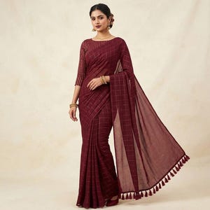 May include: A deep maroon saree featuring a subtle grid pattern in a lighter shade. The garment includes a matching long-sleeved blouse with vertical stripes and a draped section finished with decorative tassels along the bottom edge.