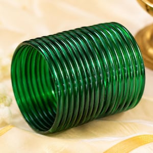 May include: A stack of multiple circular emerald green bangles made of a smooth, translucent material. The bangles are arranged in a cylindrical formation, showcasing a consistent deep green color and a polished, reflective surface throughout.