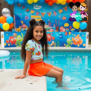 May include: A young girl wearing a light blue crop top with a Nemo design and an orange skirt sits by a pool. The background features a Disney-themed party with balloons and a banner. The image includes the text "Rae + Sea" and "Est. 2020".