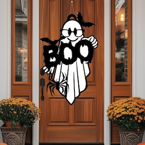 May include: A black and white Halloween ghost-shaped door decoration with the word "BOO" and a spider. The ghost wears glasses and has bat wings. The door is brown, and the porch is decorated with pumpkins and chrysanthemums.