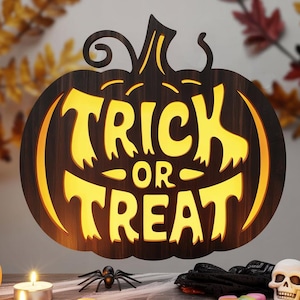 Puede incluir: Un letrero de madera con forma de calabaza con las palabras "TRICK OR TREAT" iluminadas en amarillo. La exhibición temática de Halloween incluye calabazas, calaveras, arañas, velas y caramelos sobre una mesa de madera. Hojas de otoño en el fondo.