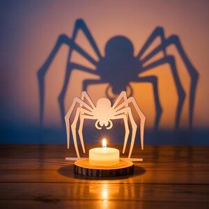 Könnte beinhalten: Ein Halloween-Kerzenhalter mit einem weißen Holzspinnen-Design. Eine brennende Kerze steht auf einem Holzsockel und wirft einen großen Spinnenschatten auf den Hintergrund. Die Kerzenflamme leuchtet hell vor dem dunklen Hintergrund.