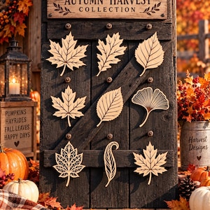 May include: A dark wooden board displays the text AUTUMN HARVEST COLLECTION and features nine distinct laser-cut wooden leaf shapes arranged in three rows. The leaves include various maple, oak, birch, and ginkgo designs with intricate cut-out details.