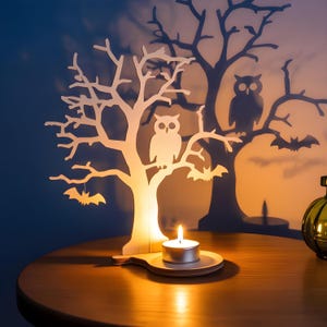 May include: A wooden Halloween-themed candle holder shaped like a tree, with an owl and bats. A lit tea light candle sits on a wooden base. The tree casts a shadow on the wall, with another owl and bats.