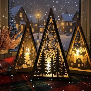 Puede incluir: Tres faroles de madera con forma de árbol de Navidad con intrincados diseños recortados. Cada farol presenta una escena invernal diferente, incluyendo árboles, copos de nieve y un reno. Los faroles están iluminados desde dentro.