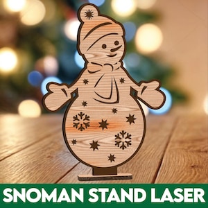 May include: A wooden snowman stand cutout with a brown wood grain finish. The snowman has a black hat, a black scarf, and a black smile. The snowman is decorated with white snowflakes and stars.