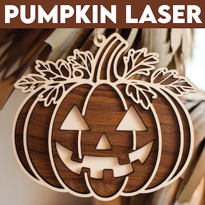 Puede incluir: Una calabaza de madera con una cara de calabaza tallada. La calabaza es marrón y tiene una textura de veta de madera. Tiene un lazo en la parte superior para colgar.