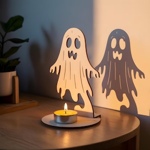 May include: A wooden ghost-shaped candle holder with a lit tea light. The ghost has cut-out eyes and a mouth, with a matching shadow on the wall. The candle holder is on a wooden base, creating a spooky Halloween decoration.