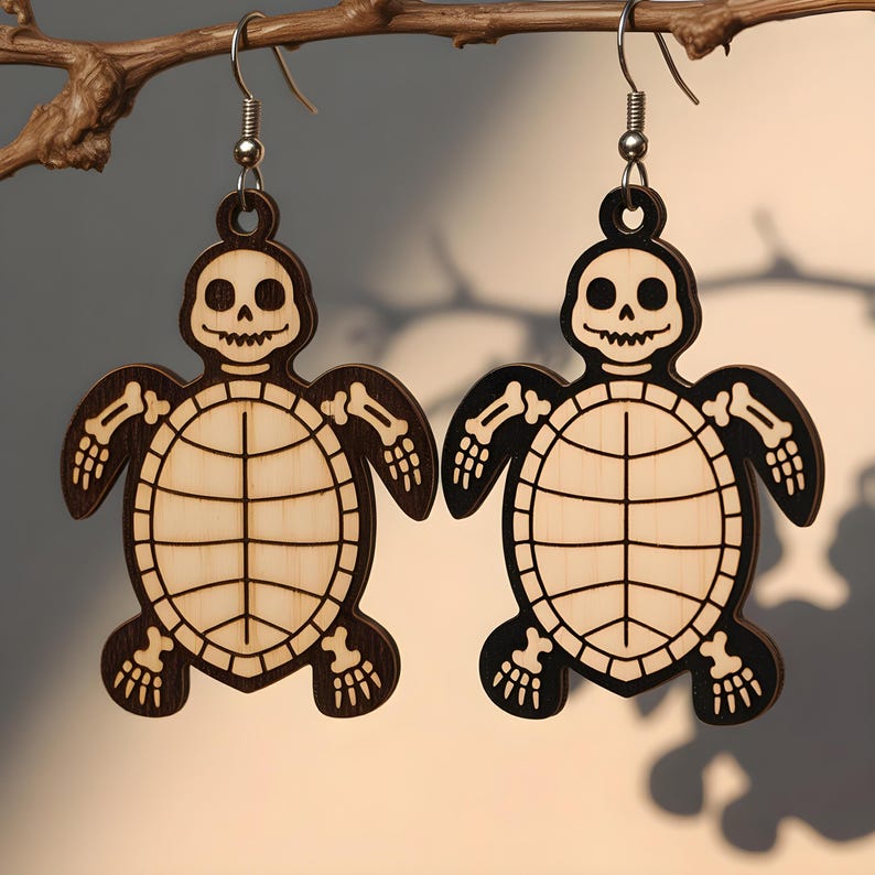 May include: A pair of wooden earrings featuring a skeleton turtle design. The earrings are laser-cut with a light wood center and dark brown outline, including the turtle's shell, head, and limbs. The earrings hang from silver-colored fish hook ear wires.