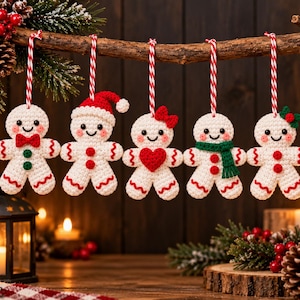 Peut inclure: Cinq décorations en crochet en forme de bonhomme en pain d'épice suspendues à une branche en bois. Chaque figurine blanc cassé a un visage souriant, des joues roses et des boucles de suspension rayées rouge et blanc, avec des accessoires variés comme un nœud rouge, un bonnet de Père Noël, un cœur rouge, une écharpe verte et une feuille de houx.